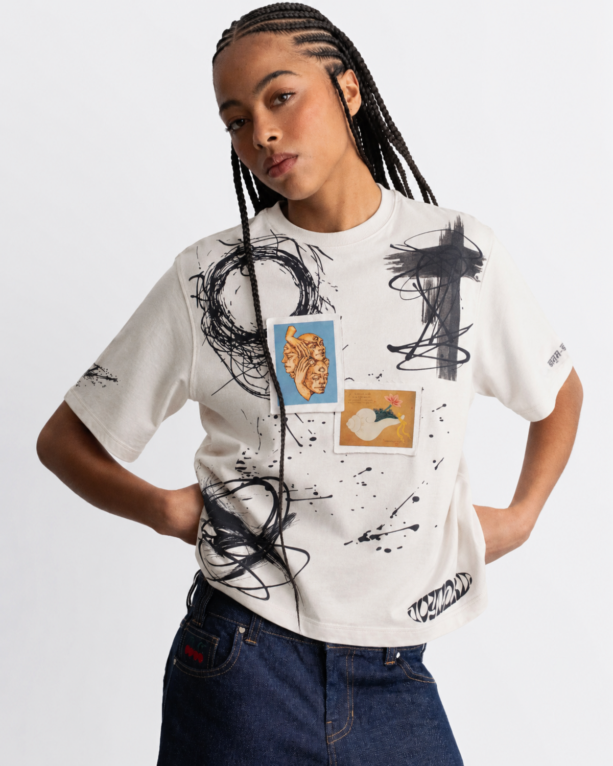 A model wearing a white graphic t-shirt with black paint splatters and abstract art prints, paired with dark blue jeans, against a plain white background.