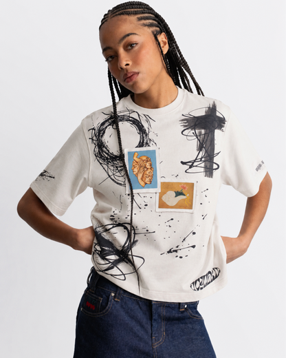 A model wearing a white graphic t-shirt with black paint splatters and abstract art prints, paired with dark blue jeans, against a plain white background.