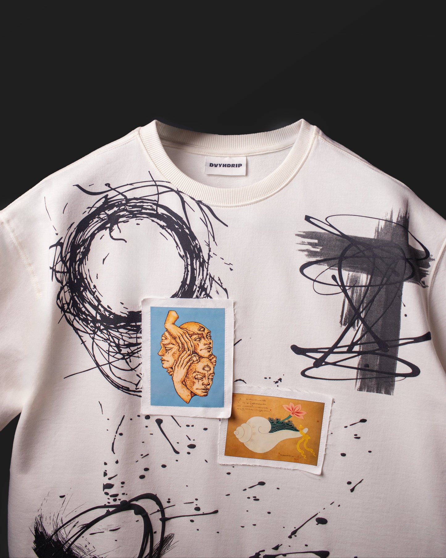 Front chest detail of the DVYNDRIP Creator T-shirt with abstract brush graphics and stitched artwork patches