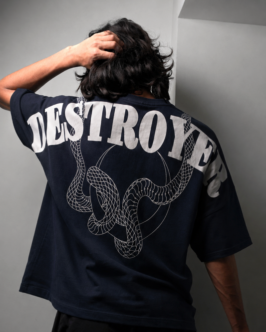 A person shown from behind wearing a dark navy blue oversized T-shirt with a large white graphic print reading 'DESTROYER' and a coiled snake design on the back, paired with black shorts against a plain white wall.