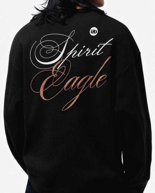 A person viewed from the back wearing a black waffle t-shirt with large decorative text on the back reading 'Spirit Eagle', plus a small circular logo near the upper back.